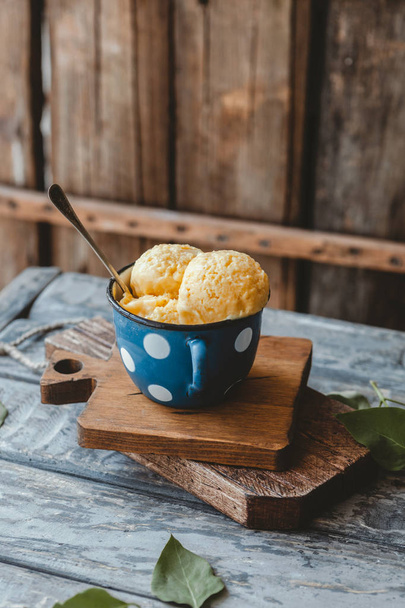 fresh mango sorbet in blue metal mug with spoon on wooden board, healthy vegan dessert - Foto, imagen
