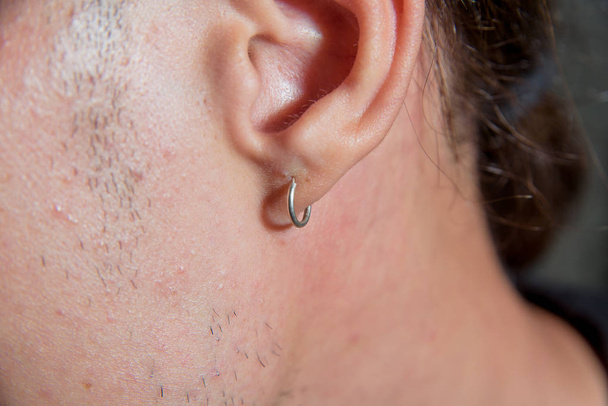 Серьги крупным планом. Небольшая серьга проколола мужское ухо. Парень с проколотыми ушами
 - Фото, изображение