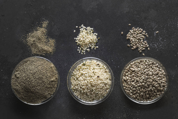 Organic dried hemp seeds , flour, kernels in black bowls on dark background. View from above. - Photo, Image