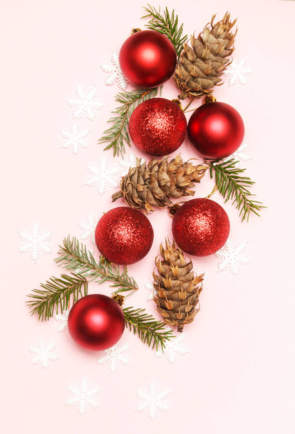 淡いピンクの背景に赤いクリスマスの光沢のあるボールとモミの小枝。クリスマスオーナメントのアレンジ. - 写真・画像
