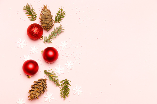 淡いピンクの背景に赤いクリスマスの光沢のあるボールとモミの小枝。クリスマスオーナメントのアレンジ. - 写真・画像