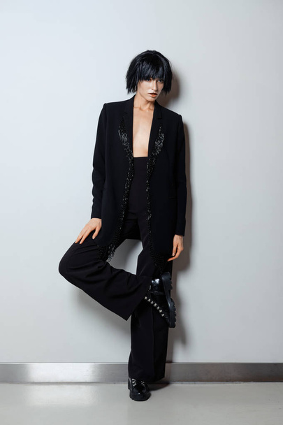 Fashion model in black wig, pantsuit with beaded fringe and rough doots with lacing - Фото, зображення