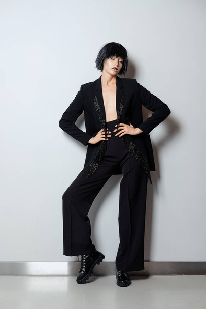 Fashion model in black wig, pantsuit with beaded fringe and rough doots with lacing - Fotoğraf, Görsel