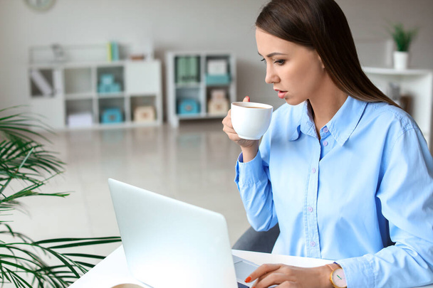 Fiatal nő kávézik, miközben az irodában dolgozik - Fotó, kép