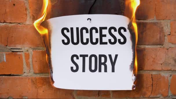 Beyaz bir A4 tablosundaki yazı turuncu bir duvarın arka planına karşı. İçinde "Başarı Hikayesi" yazan gazete yanıyor, duman çıkıyor ve küle dönüşüyor. İş konsepti. - Video, Çekim