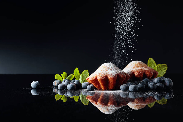 Muffins sprinkled with sugar powder on a black reflective backgr - Photo, Image