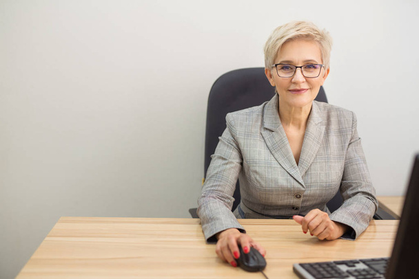adult woman in a suit and glasses at a table indoors at a computer - Photo, image