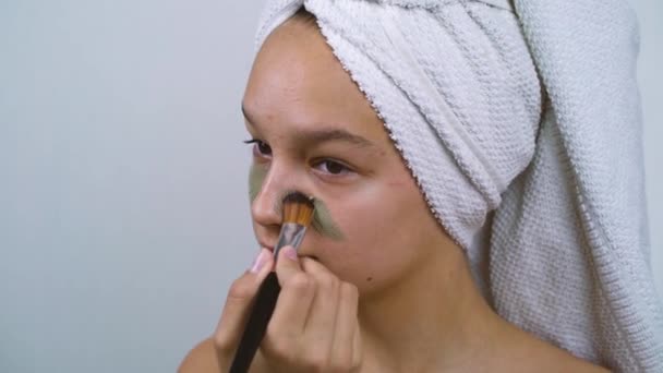 Teenage girl with skin problems applying facial clay mask at home spa - Metraje, vídeo