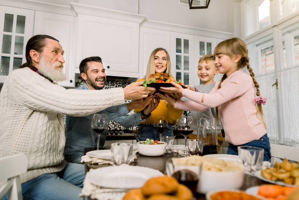 hübsche junge Mutter mit köstlichem Truthahn für das Weihnachtsessen mit der Familie. Kinder, Vater und Großvater freuen sich und halten die Hände auf dem Teller mit Truthahn. Leckeres Essen, Abendessen - Foto, Bild