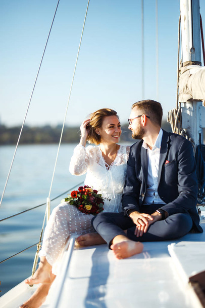 Beautiful wedding couple on yacht at wedding day outdoors in the sea. Beautiful elegant  bride in a white dress and stylish groom on the luxury yacht sailing down the sea. Together. Wedding day. - Fotó, kép