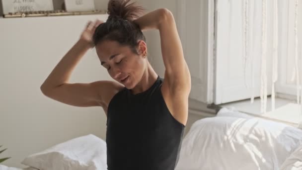 Pleased pretty asian woman wakes up and stretch oneself with closed eyes while sitting on bed at home - Materiaali, video