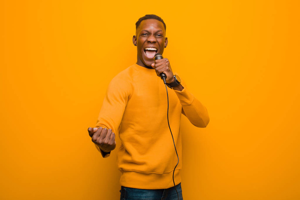 young african american black man against orange wall with a microphone - Foto, Imagen