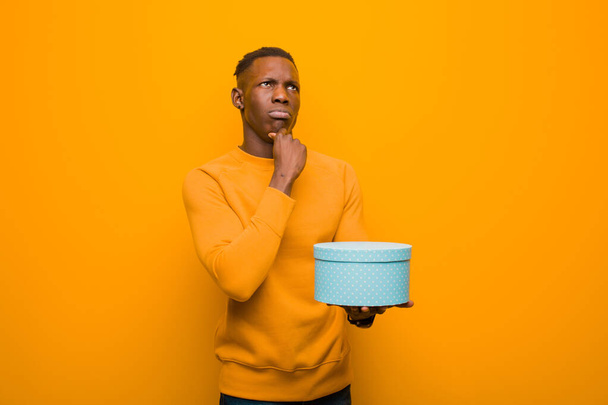 young african american black man against orange wall with a gift - Foto, Imagem