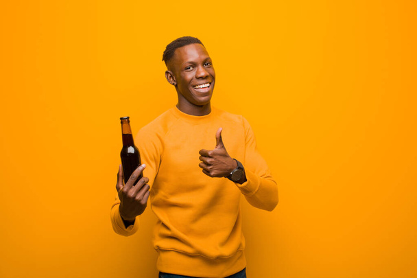 jeune homme noir afro-américain contre le mur d'orange ayant une bière
 - Photo, image