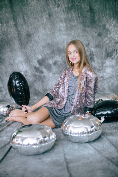 Attractive young girl with blond hair and evening make-up in a silver dress and metallized silver and black balloons. - Foto, Imagem