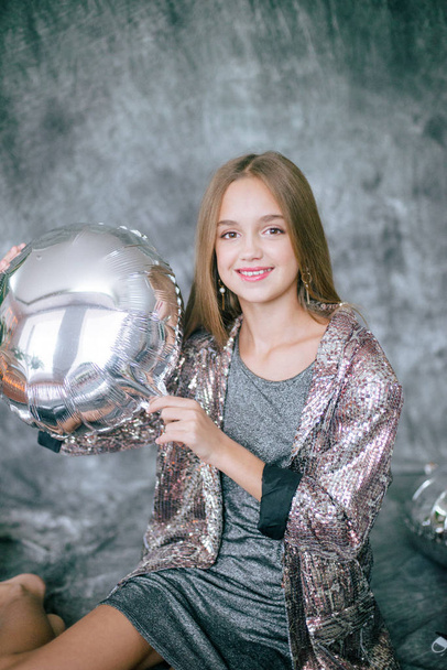Attractive young girl with blond hair and evening make-up in a silver dress and metallized silver and black balloons. - Zdjęcie, obraz