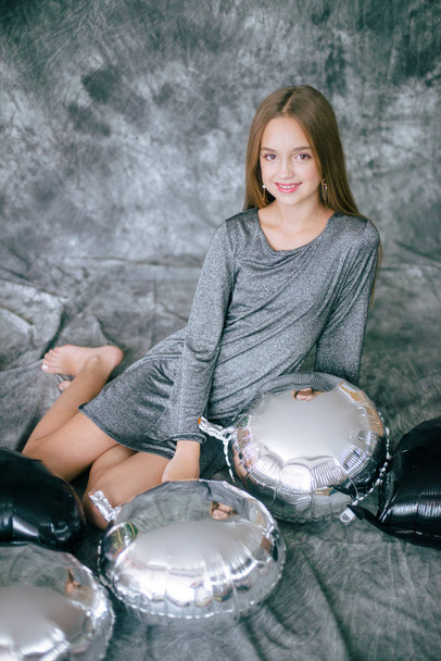 Attractive young girl with blond hair and evening make-up in a silver dress and metallized silver and black balloons. - 写真・画像
