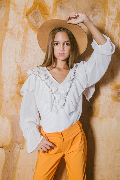 Attractive young girl with blond hair and evening make-up in retro flared pants and a chiffon boho blouse and hat - Foto, imagen