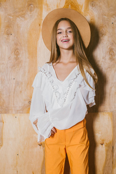 Attractive young girl with blond hair and evening make-up in retro flared pants and a chiffon boho blouse and hat - Foto, immagini