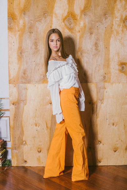 Attractive young girl with blond hair and evening make-up in retro flared pants and a chiffon boho blouse and hat - Valokuva, kuva