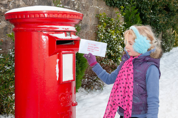 Νεαρή κοπέλα σε μια χιονισμένη σκηνή έτοιμη να στείλει το Χριστουγεννιάτικο γράμμα της στον Άγιο Βασίλη. - Φωτογραφία, εικόνα