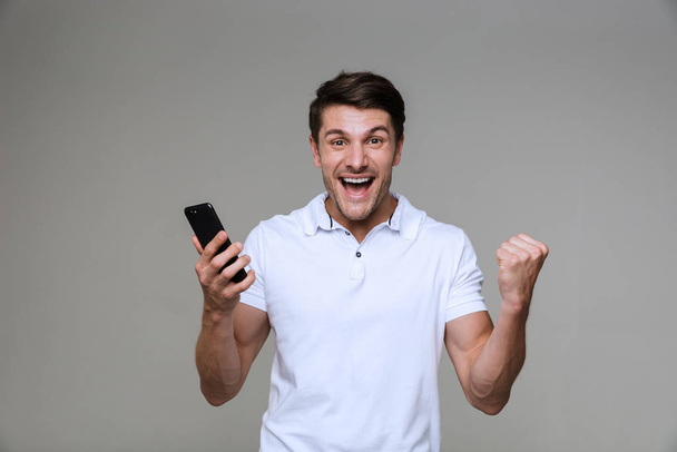 Emotional young man using mobile phone make winner gesture. - Fotografie, Obrázek