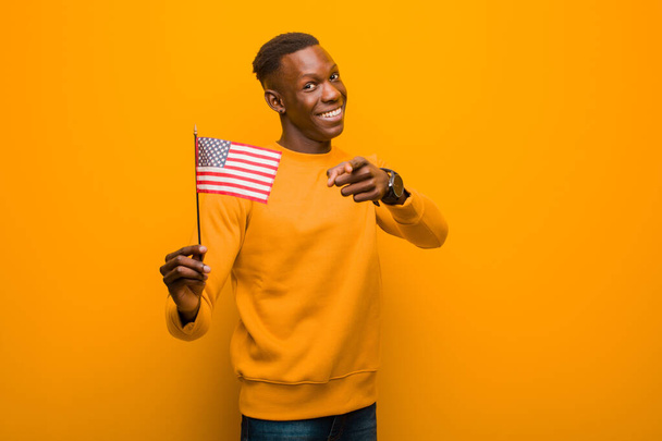 young african american black man against orange wall holding an usa flag - Fotó, kép