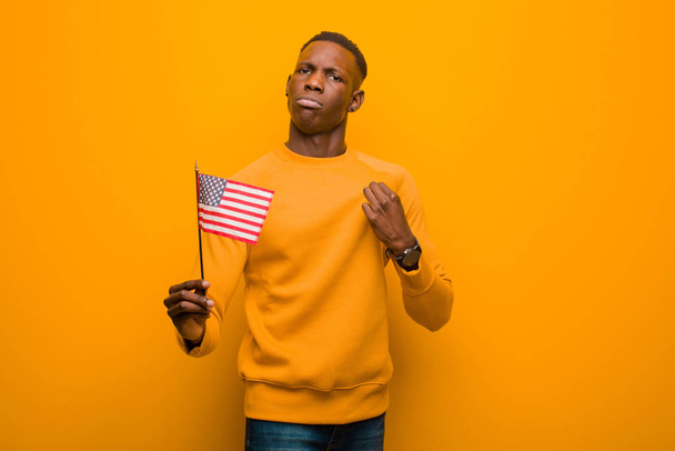 young african american black man against orange wall holding an usa flag - Foto, Imagem