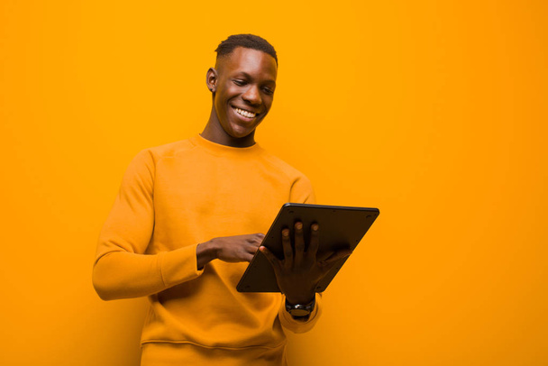 young african american black man against orange wall with a smart tablet - Foto, immagini