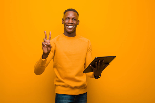 young african american black man against orange wall with a smart tablet - Photo, Image
