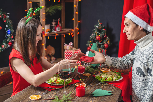 Casal jovem de amantes estão gastando um jantar festivo de Natal. Marido faz sua esposa uma surpresa dando um presente de ano novo
 - Foto, Imagem