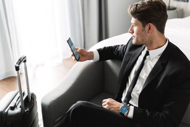 Image of caucasian young man sitting on sofa with smartphone and - Photo, image