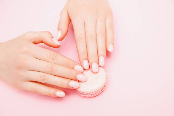 Stijlvolle trendy vrouwelijke manicure op roze achtergrond. Meisje houdt hand in hand macaron koekjes. Bovenaanzicht, vlak lay - Foto, afbeelding
