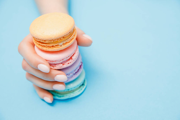 Menina de mão de beleza com manicure na moda tomando macarons de cor no fundo azul
 - Foto, Imagem