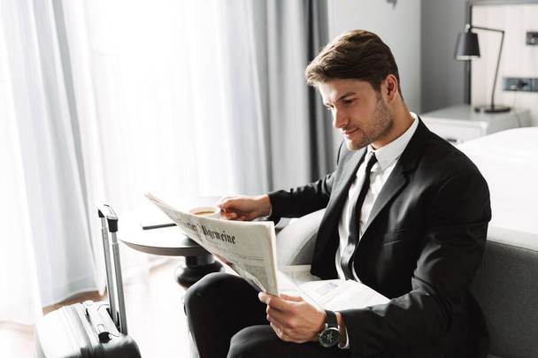 Concentrated serious businessman indoors at home reading newspaper drinking coffee. - 写真・画像