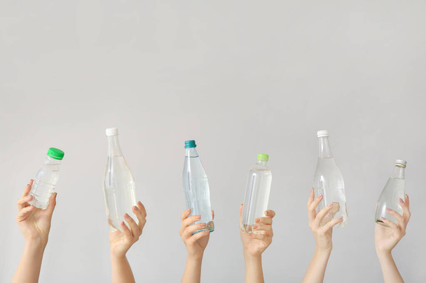 Female hands with bottles of water on grey background - Фото, изображение