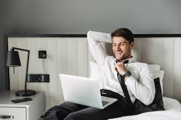 Image of happy young man lying on bed with laptop computer in ho - Foto, immagini