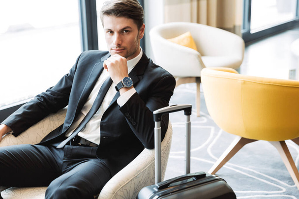 Photo of unshaven young businessman wearing formal black suit si - Photo, image