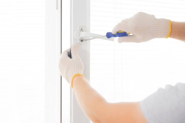 Construction worker man uses screwdriver to screw handle install plastic white upvc windows in house - Foto, afbeelding