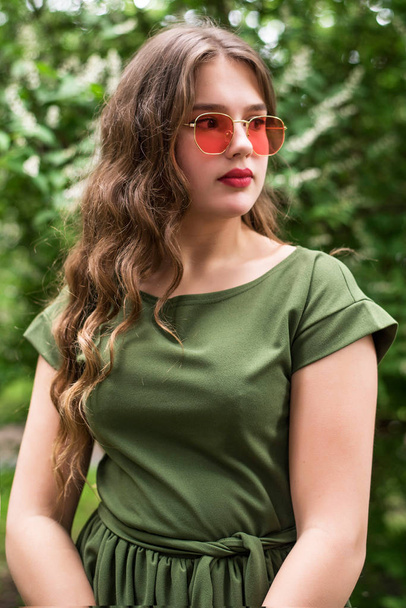 Портрет молодой девушки в зеленом платье и красных солнечных очках. Закрывай. Плюс модель размера
. - Фото, изображение