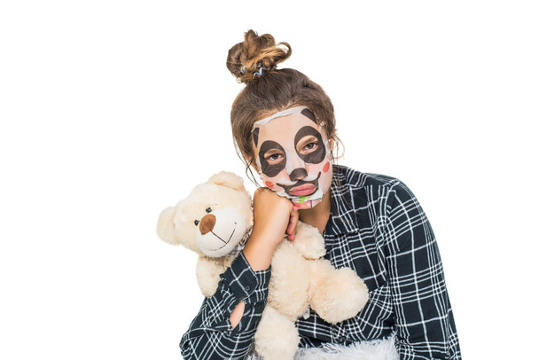 junges Teenager-Mädchen mit Panda-Gesichtsmaske, das isoliert auf weißem Hintergrund in die Kamera blickt. kosmetischer Eingriff. Beauty Spa und Kosmetologie. - Foto, Bild