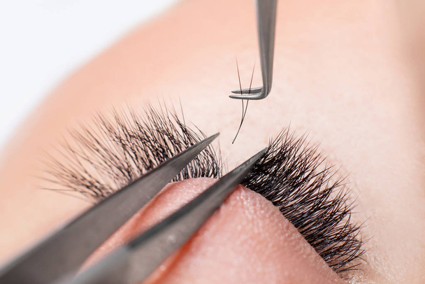 Eyelash extension procedure. Master tweezers fake long lashes beautiful female eyes - Foto, Imagem