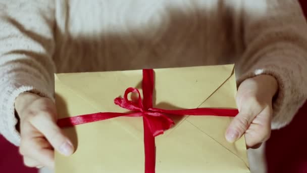 Beautiful girl hands hold a gift envelope with a red ribbon. Beautiful girl holds out a gift envelope with a red ribbon. Gift for the holiday. Happy New Year, Merry Christmas, Happy Valentines Day. - Séquence, vidéo