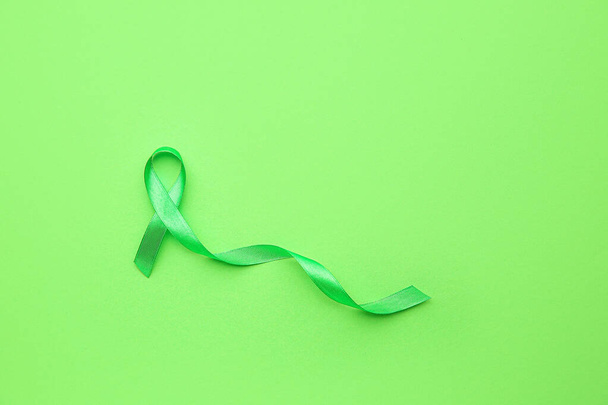 Green ribbon on color background. Cancer awareness concept - Photo, Image