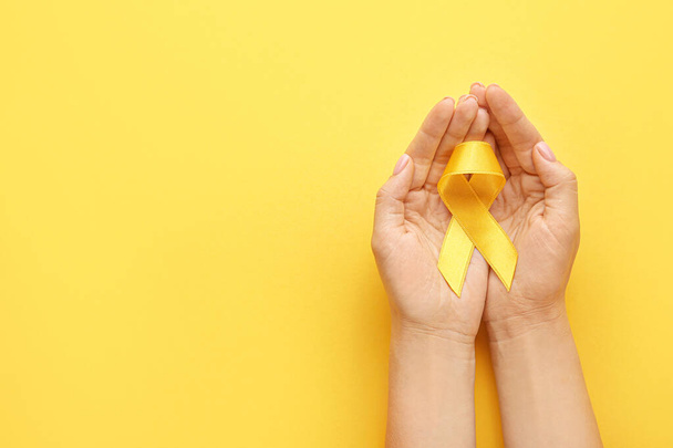 Female hands with yellow ribbon on color background. Cancer awareness concept - Photo, image