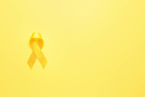 Κίτρινη κορδέλα σε φόντο χρώματος. Έννοια ευαισθητοποίησης για τον καρκίνο - Φωτογραφία, εικόνα