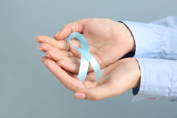 Female hands with blue ribbon on grey background. Cancer awareness concept - Фото, изображение
