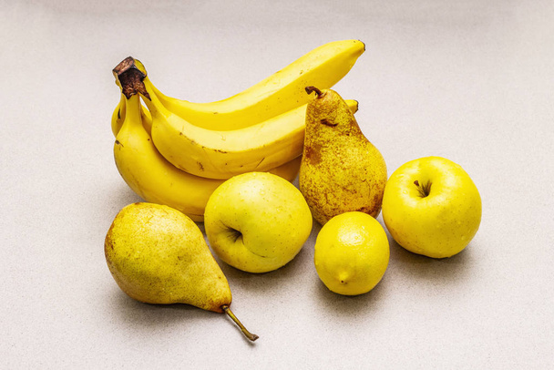 Geassorteerde felgele vruchten. Verse banaan, peer, appel, citroen. Oogst op een stenen achtergrond - Foto, afbeelding