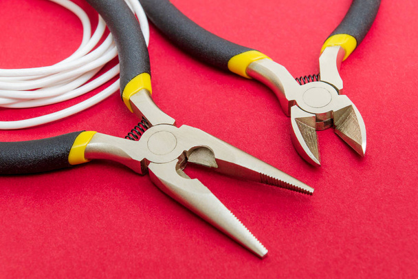 Alicates ferramenta e fios para eletricista close-up no fundo vermelho
 - Foto, Imagem