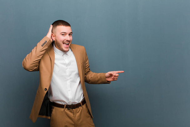 young handsome businessman laughing, looking happy, positive and surprised, realizing a great idea pointing to lateral copy space against flat background - Foto, Imagem